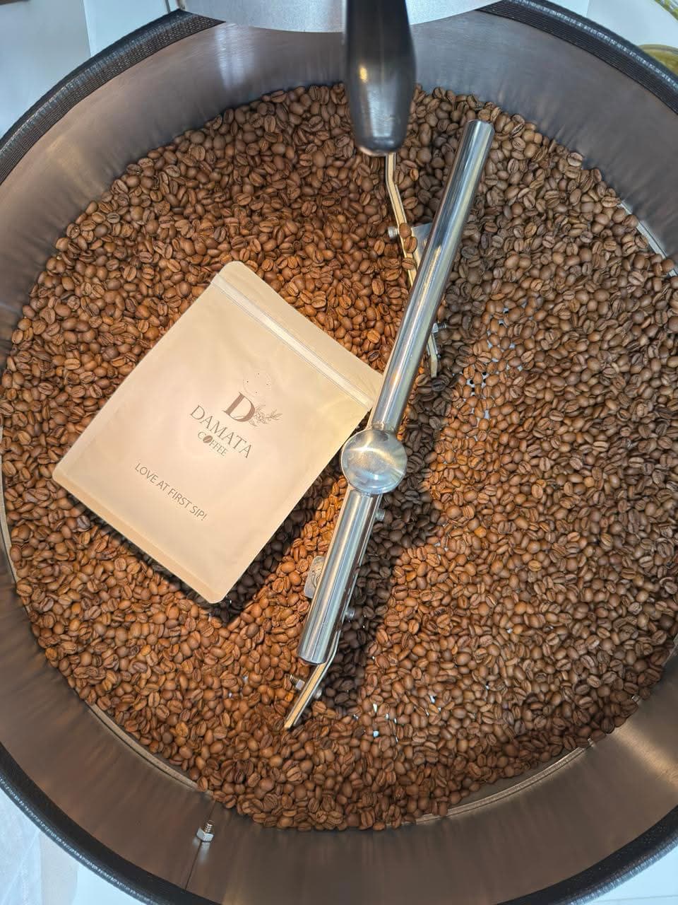 A Damata coffee bag resting in the roasting drum among freshly roasted beans